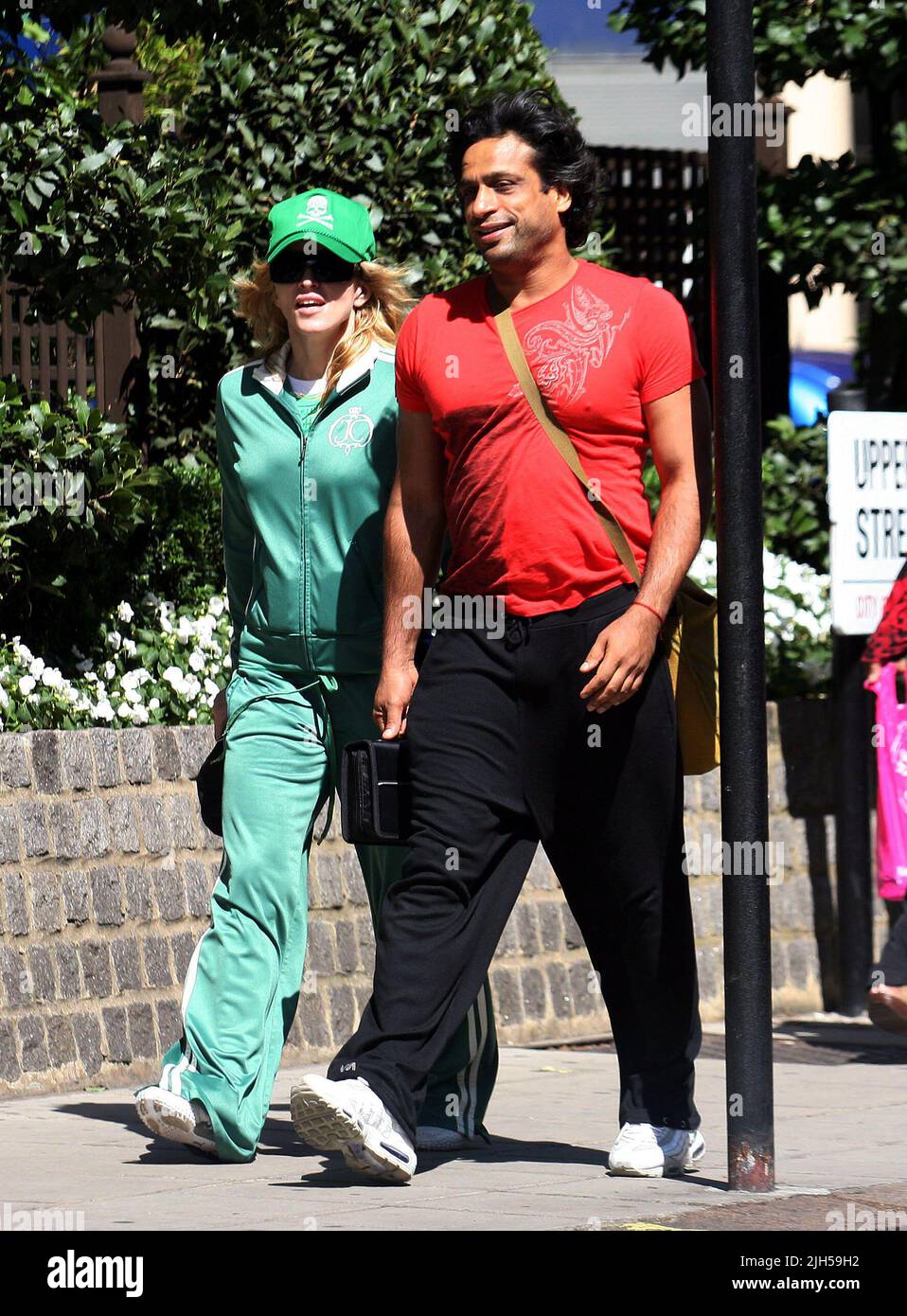 **EXCLUSIVE**PICTURES**TRUE**GREEN!** MADONNA STROLLS OUT FOR LUNCH WITH HER FITNESS/GYROTRONIC GURU JAMES D'SILVA NEAR HER LONDON MANSION TODAY SPORTING A SKULL AND CROSSBONE MOTIF BASEBALL CAP WITH MATCHING TRACKSUIT. Stock Photo