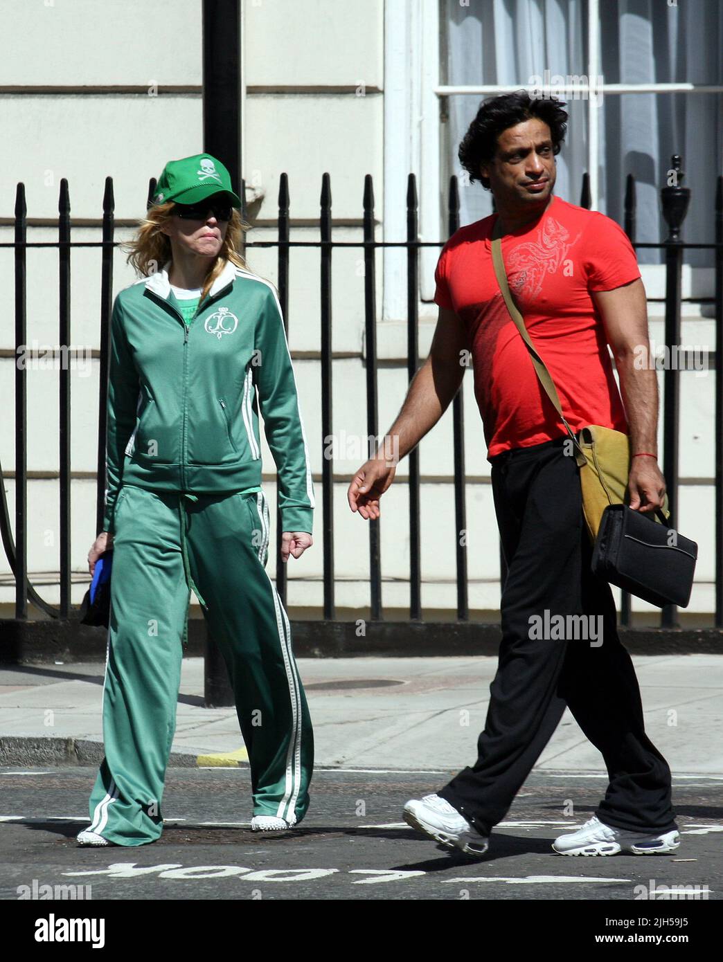 **EXCLUSIVE**PICTURES**TRUE**GREEN!** MADONNA STROLLS OUT FOR LUNCH WITH HER FITNESS/GYROTRONIC GURU JAMES D'SILVA NEAR HER LONDON MANSION TODAY SPORTING A SKULL AND CROSSBONE MOTIF BASEBALL CAP WITH MATCHING TRACKSUIT. MADONNA WAS CLUTCHING A BOTTLE CONTAINING A MYSTERY DRINK. Stock Photo