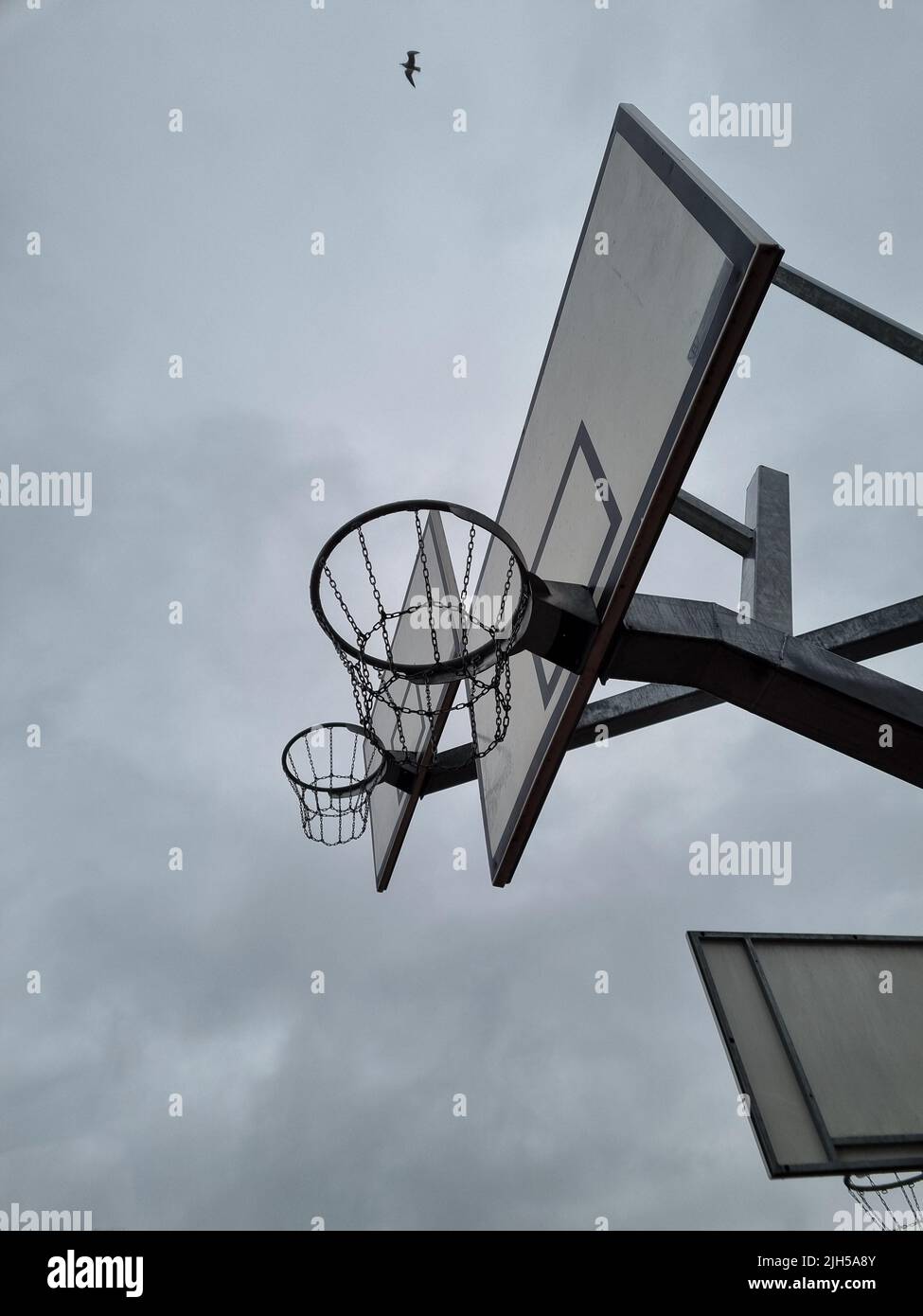 Outdoor basketball rings with chain nets at different levels. Street basketball hoop with a view from below. Street sport during overcast. Stock Photo