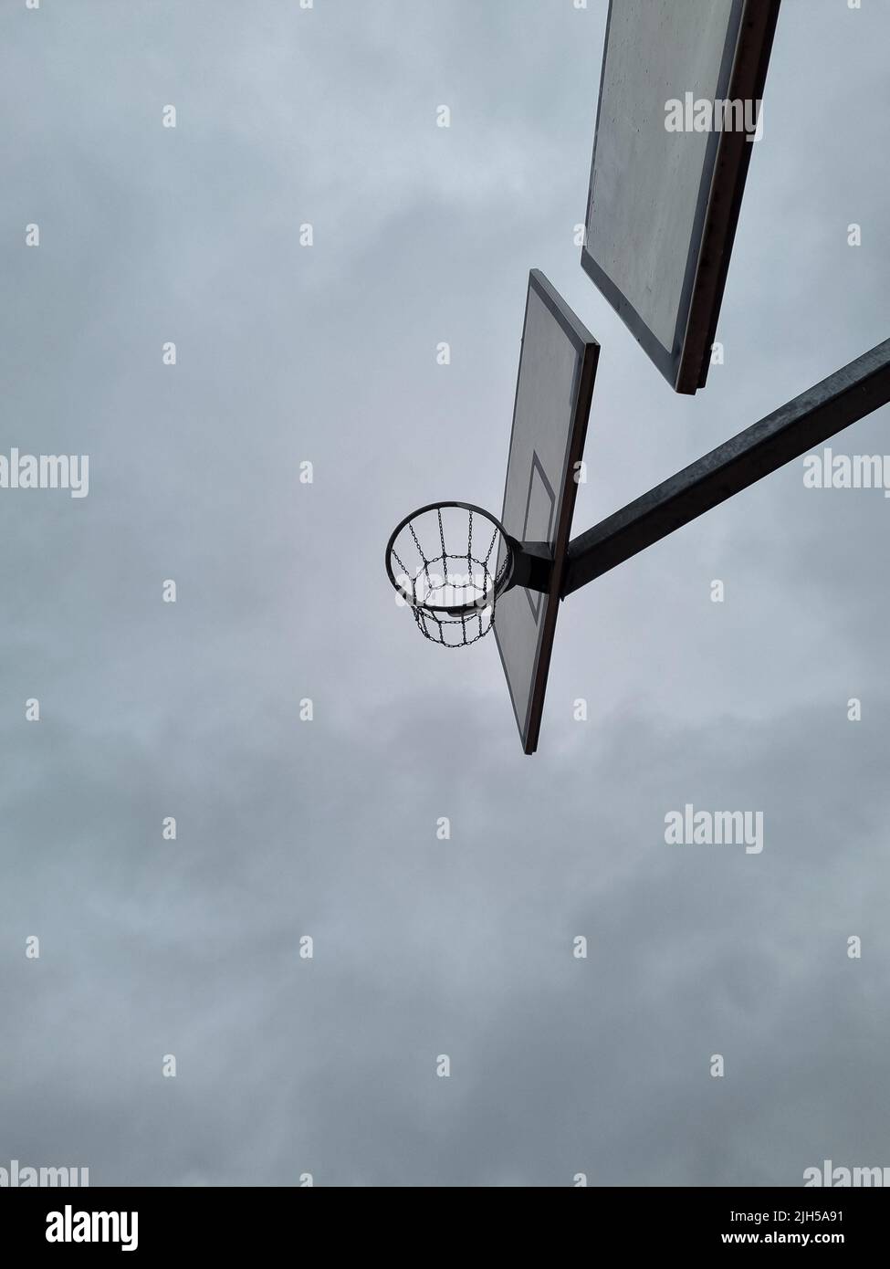 Outdoor basketball rings with chain nets at different levels. Street basketball hoop with a view from below. Street sport during overcast. Stock Photo