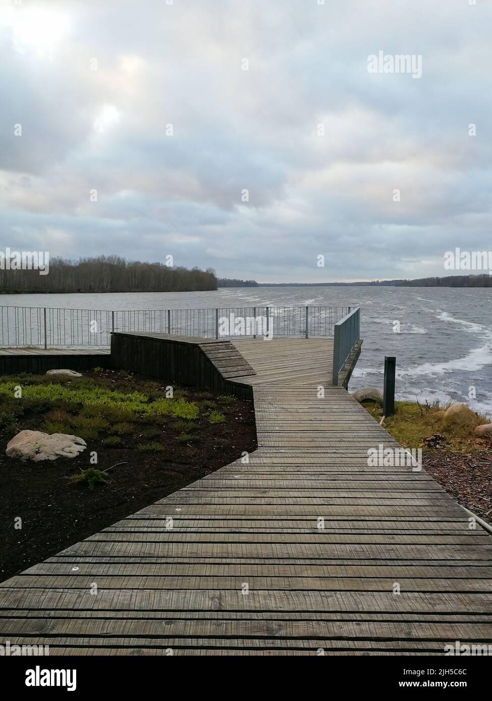 A wooden pier leads to a viewing platform. Wooden site in front of the river. Wooden walk board with a fence. Pier with balcony. Stock Photo