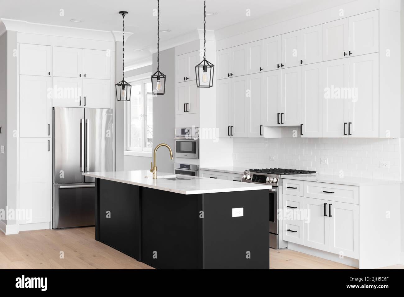 A luxury white kitchen with black pendant lights hanging above black
