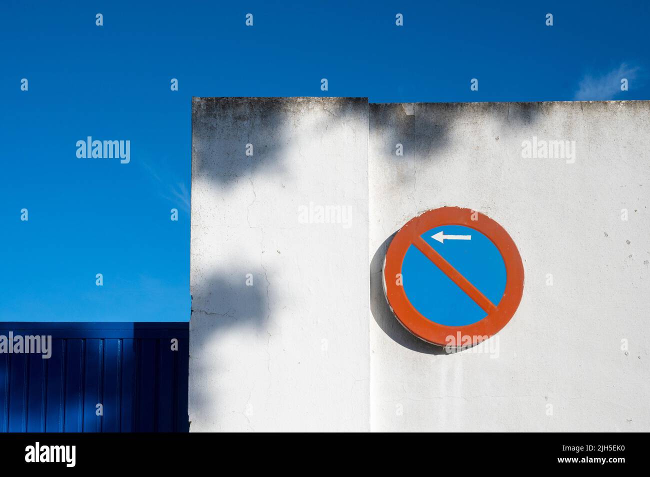 A red and blue no parking sign on a white wall in Spain with vibrant blue and red colour Stock Photo