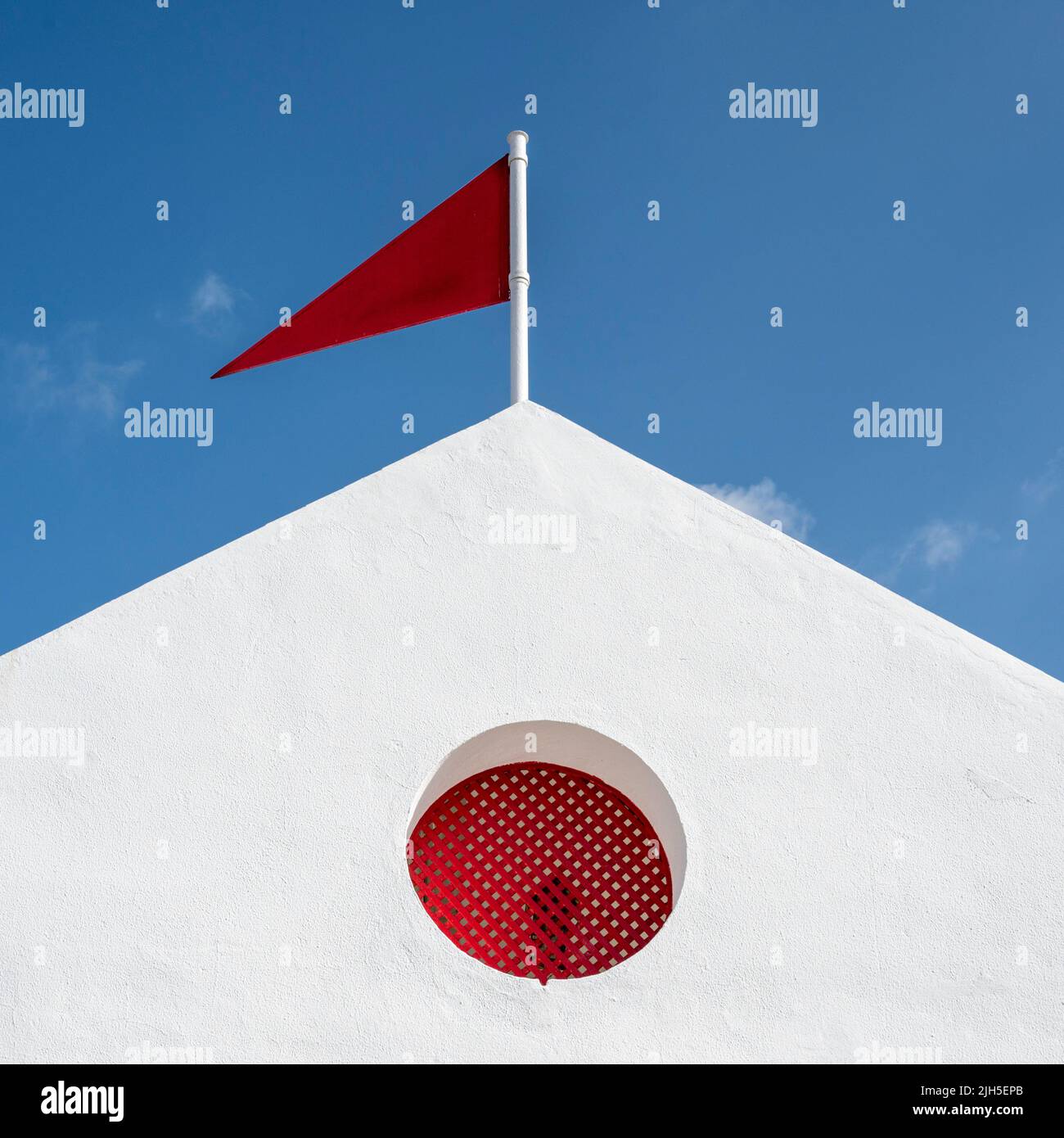 A red flag on a building in Spain against a blue sky in a colourful image of urban architecture Stock Photo
