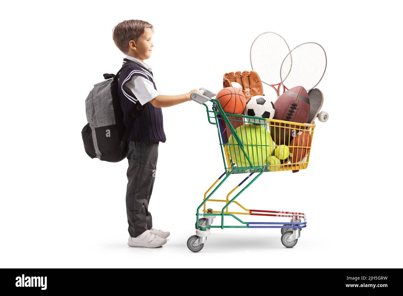 Full length profile shot of a schoolboy in a uniform with a shopping cart full of sports equipment isolated on white background Stock Photo