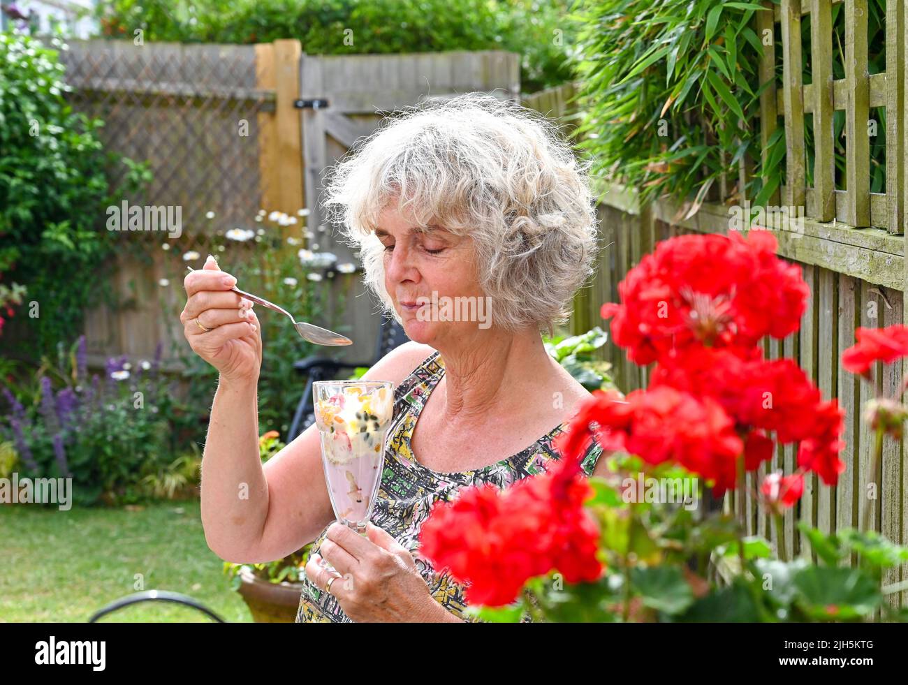 Woman eating outdoors in garden a healthy summer breakfast of yoghurt  , flakes , granola and fresh strawberries  UK Stock Photo