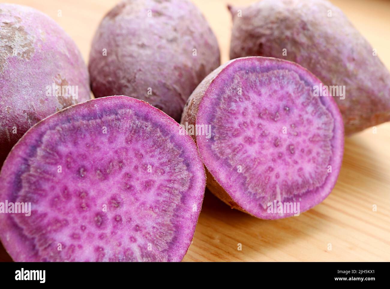 Closeup of Crosssection of Raw Purple Sweet Potatoes with Blurry Whole Roots in Backdrop Stock