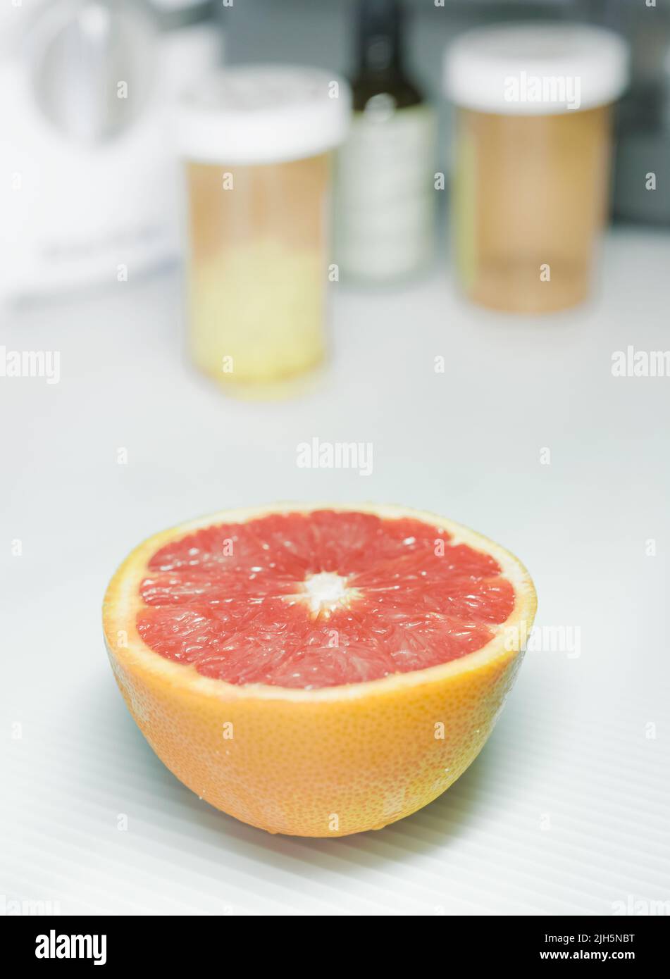 Half grapefruit in front, blurred background with some pills containers. Stock Photo