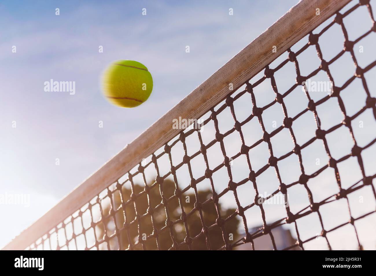 Tennis ball flies close over net, dangerous hit, ball is in motion, the sky is on background