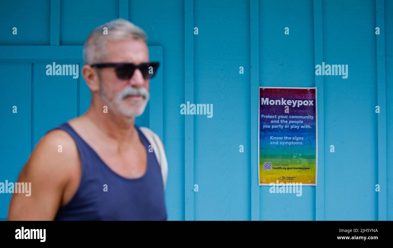 A man walks near a poster with monkeypox information at a local store at Fire Island-Cherry Grove, in New York, U.S., July 15, 2022. REUTERS/Eduardo Munoz Stock Photo