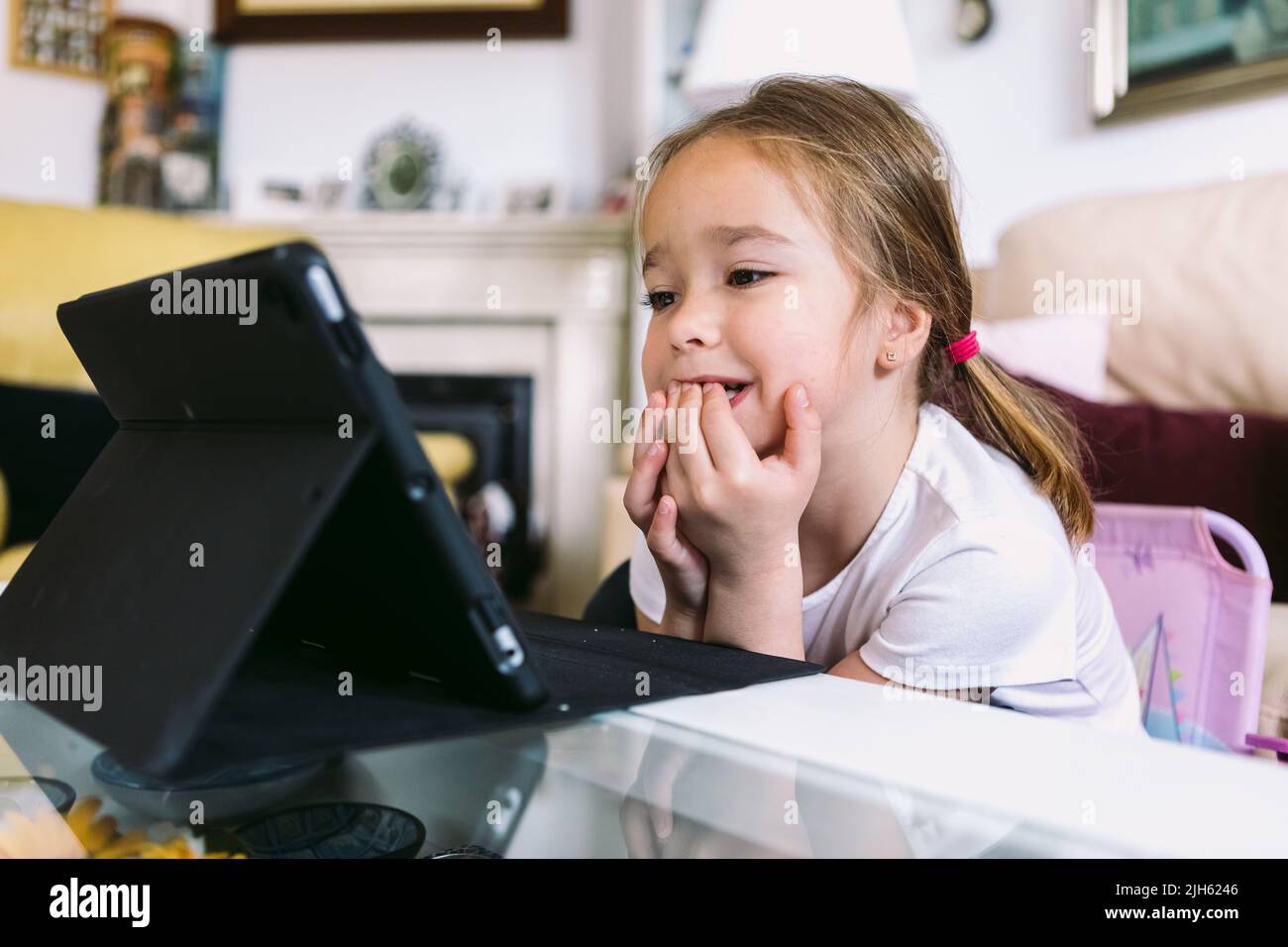 A little blonde girl intently watching a video on a tablet in her ...