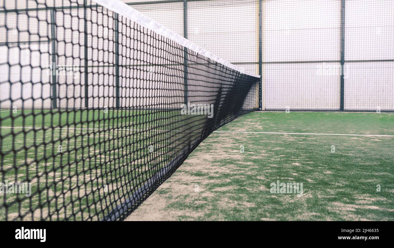 Net and a part of green synthetic grass paddle tennis court indoor without people. Paddle is a racquet game. Professional sport concept with copy spac Stock Photo