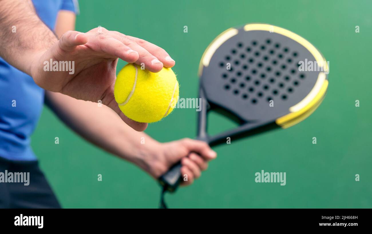 Professional monitor of padel holding a yellow ball and black racket to the open. Class to student on outdoor tennis court. Man paddel player playing Stock Photo
