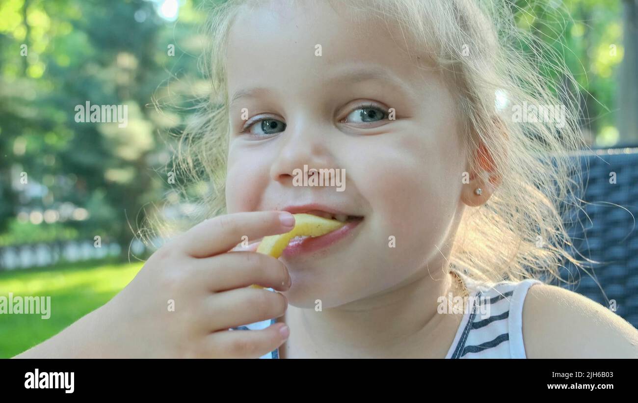 Little girl eat french fries. Close-up of blonde girl takes potato chips with her hands and tries them sitting in street cafe on the park. Odessa Stock Photo