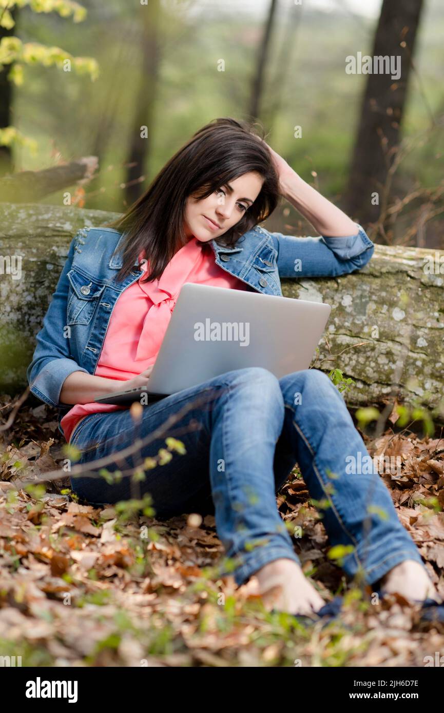 Young woman sitting in the forest with laptop Stock Photo - Alamy