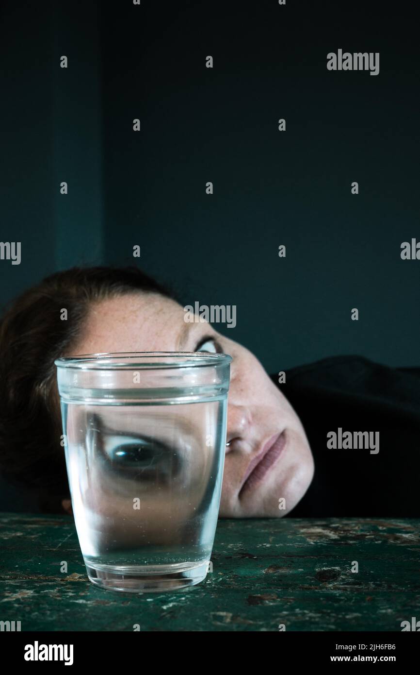 Creepy face of a woman, eye reflected in a water glass Stock Photo