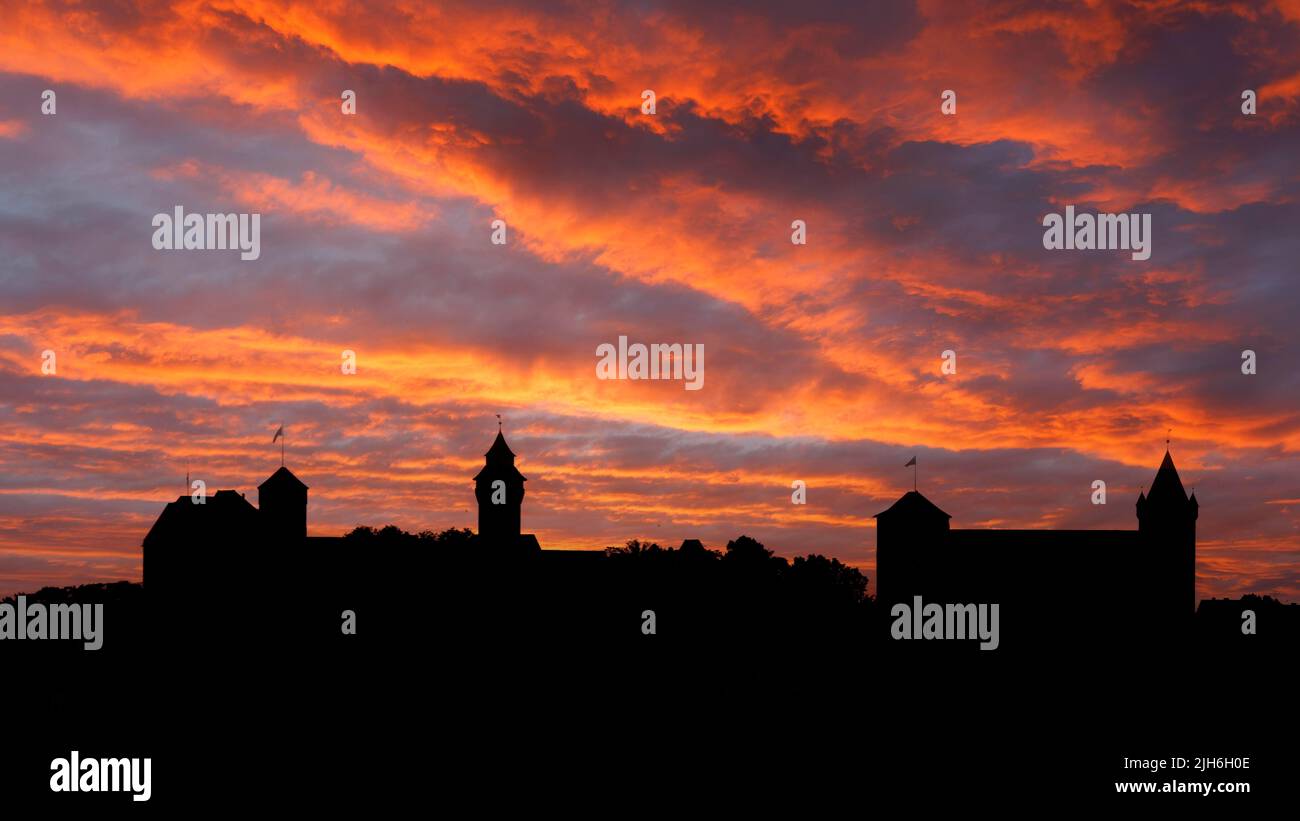 Fiery red evening sky after sunset with skyline, silhouette from left Kaiserburg with Heidenturm and Sinwellturm, right former Kaiserstallung with Stock Photo