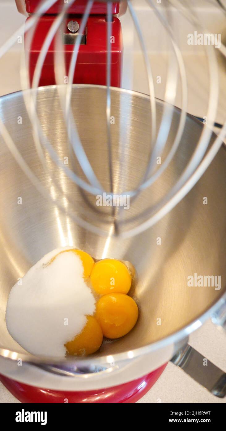 Raw eggs with sugar in a metal bowl of standing mixer. Preparing egg yolk with sugar in kitchen mixer Stock Photo