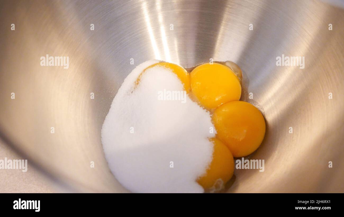 Raw eggs with sugar in a metal bowl of standing mixer. Preparing egg yolk with sugar in kitchen mixer Stock Photo