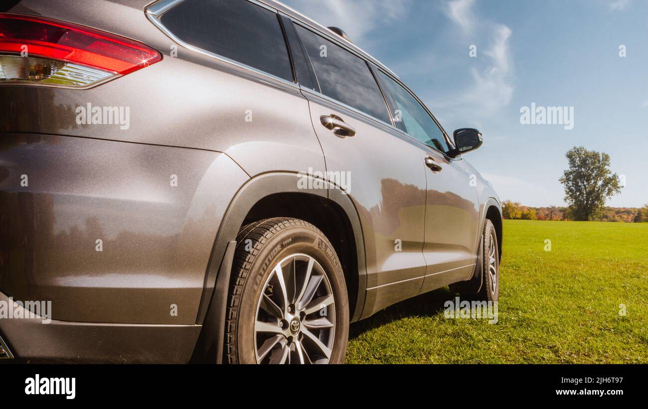 Rear side of gray car driving on the road with background of grass and country city. Parked car front side a wide field with mountains and trees in th Stock Photo