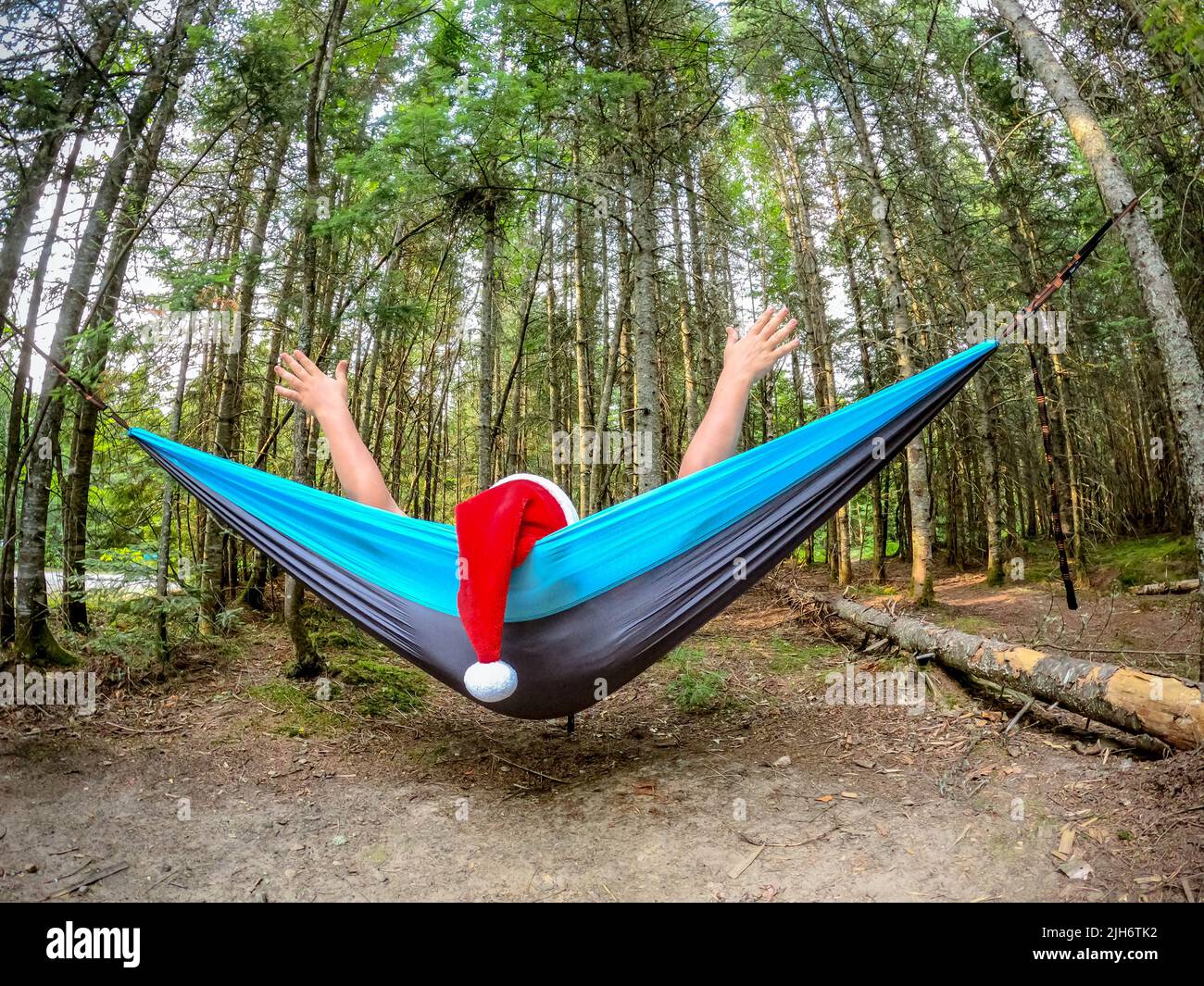 Joyful guy with Santa hat relaxed in a hammock and drinking beer in the