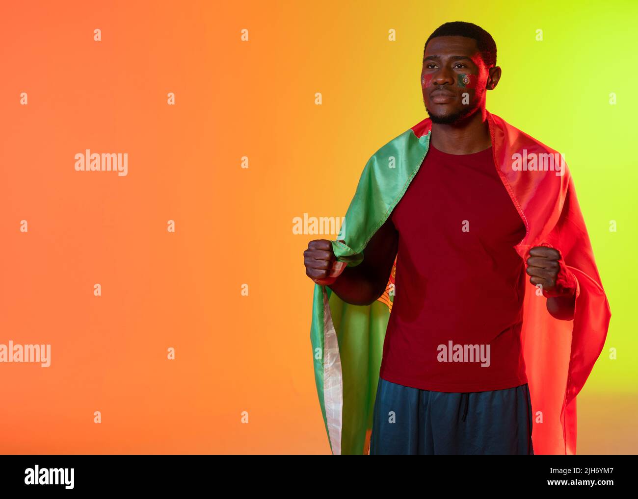 African american male football supporter with flag of portugal over orange and yellow lighting Stock Photo