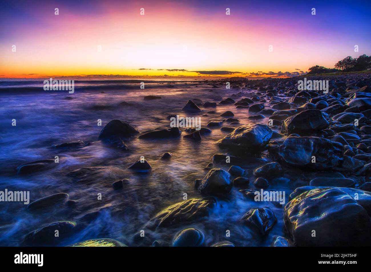Pebbles on Pebbly beach of Forster town in Australia on Pacific coast - dark scenic seascape sunrise. Stock Photo