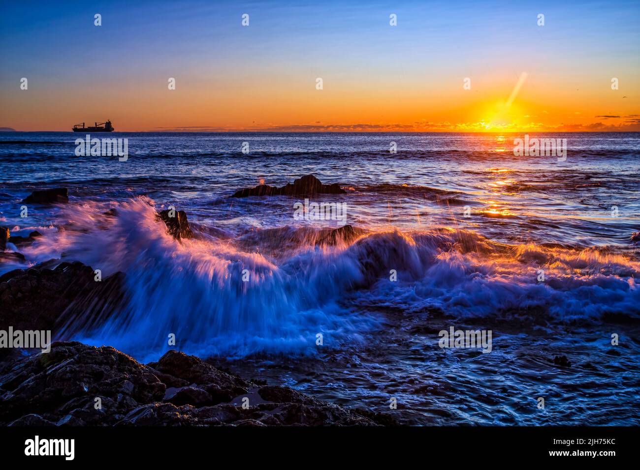 Splash of wave lit by rising sun off Pebbly beach in Forter town of Pacific ocean coast in Australia at sunrise. Stock Photo