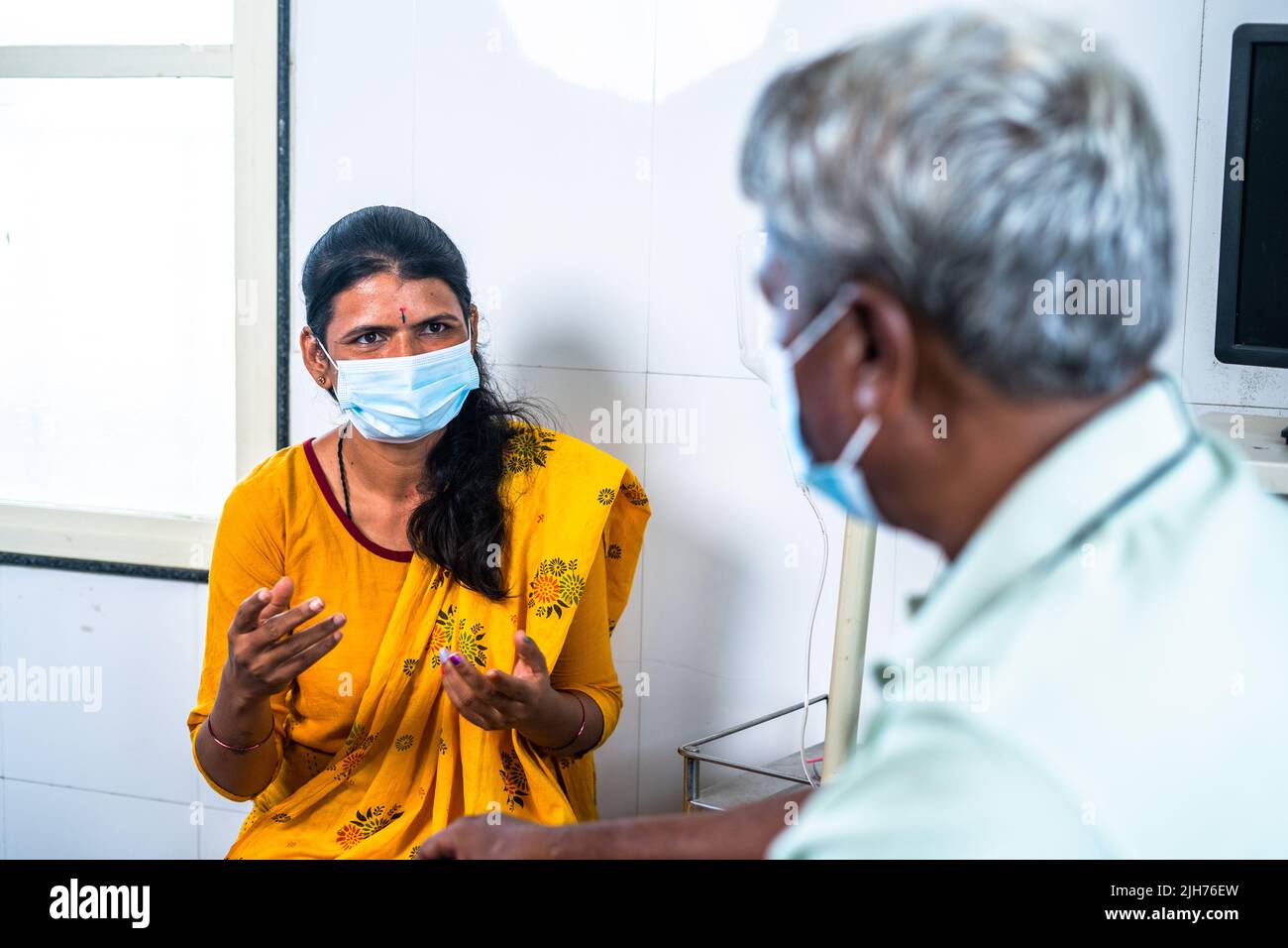 Shoulder shot of father with medical face mask talking with daughter about treatment while sitting on bed at hospital - concept of recovery, hygiene Stock Photo
