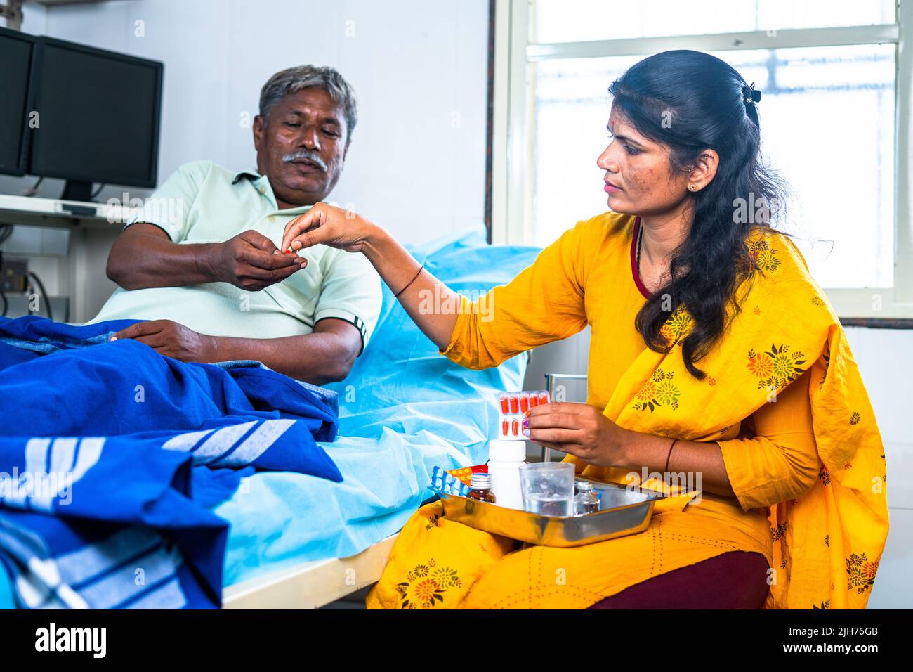 Daughter giving medicine or pills to admitted sick father at hospital - concept of family caring, medical treatment and health care. Stock Photo