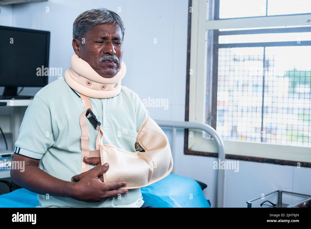 Senior man suffering from injury of neck and hand fracture while sitting on hospital bed - concept of medicare, health care treatment and safety. Stock Photo