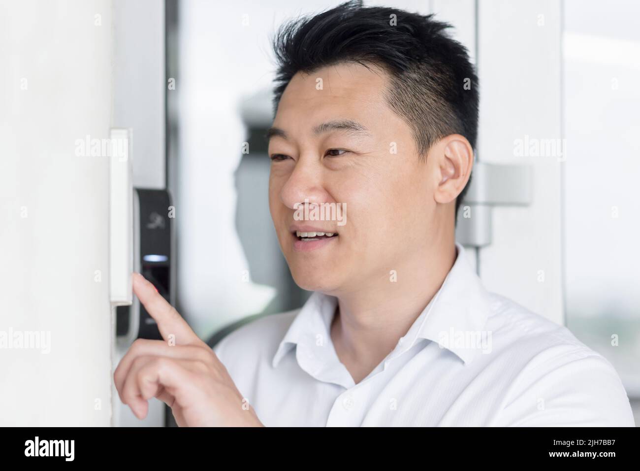 Close-up photo. Portrait of a young handsome Asian man, calling the intercom of the house, pressing the button, waiting for the door to open. Stock Photo