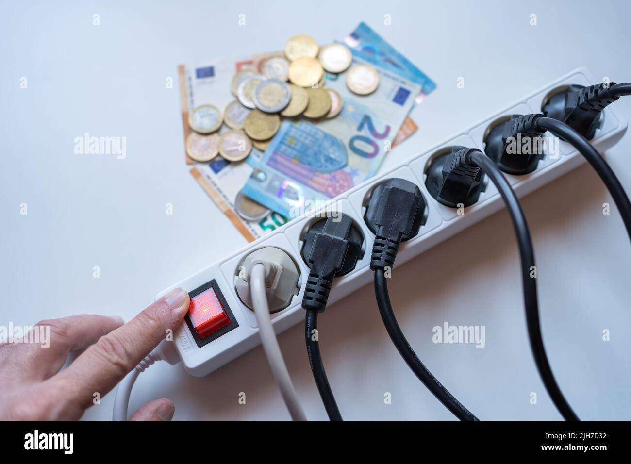 Hand of a man lighting a strip of plugs with money that represents the high cost of electricity