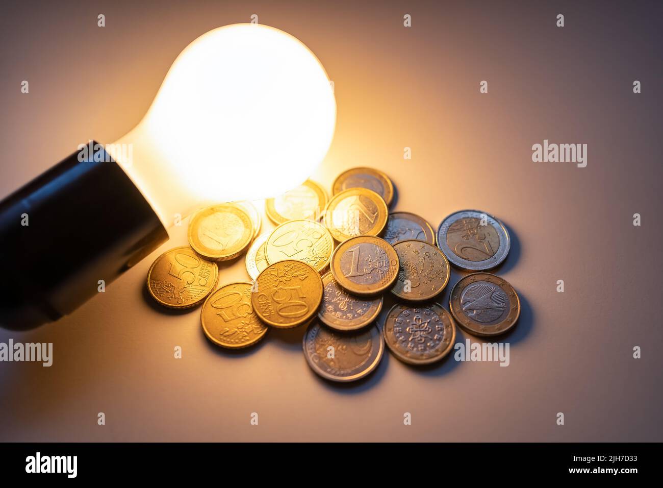 Light bulb lit illuminating coins for the high cost of electricity and