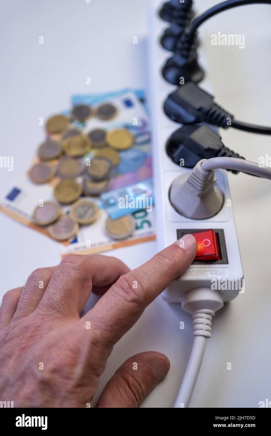 Hand of a man lighting a strip of plugs with money that represents the high cost of electricity