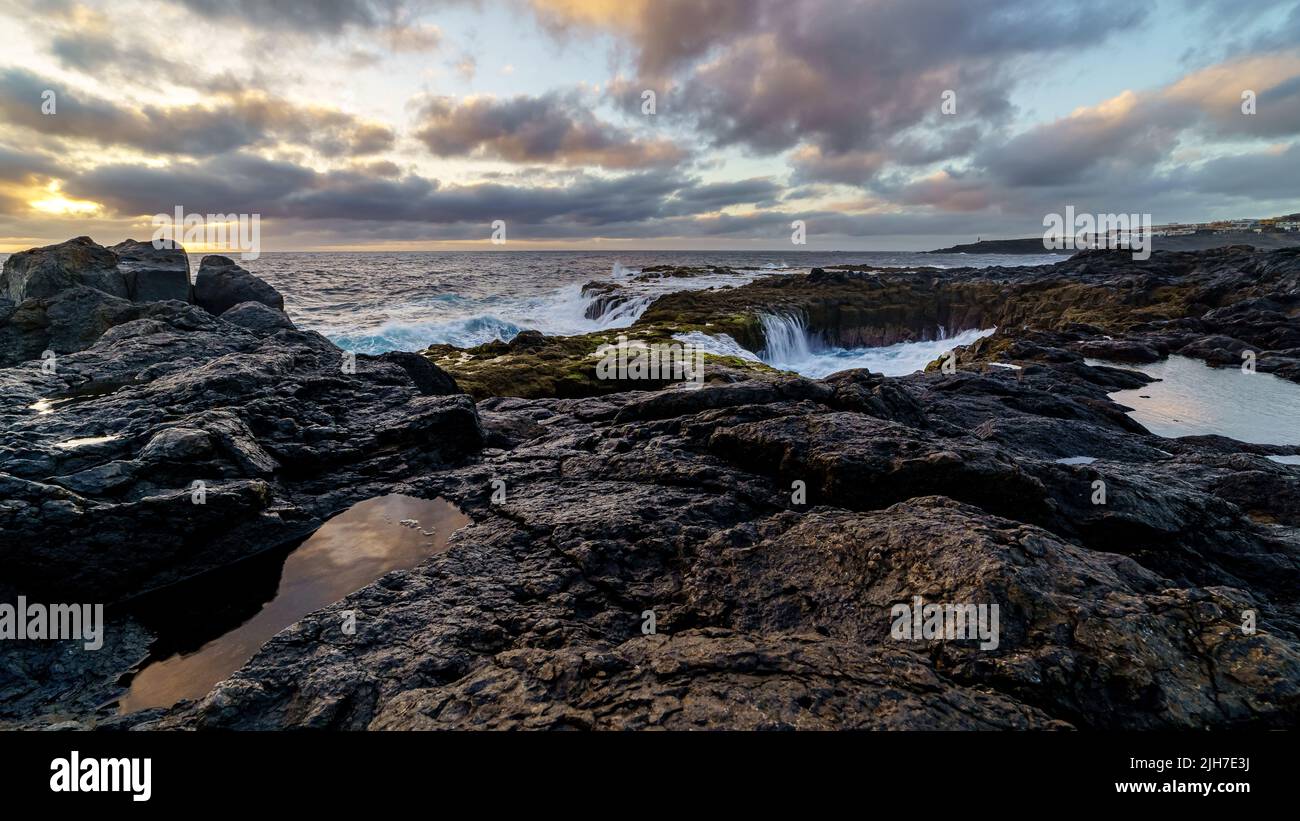 Sunset on the sea coast with large rocks washed by the waves, sky with clouds in golden tones and reflections in the water between the rocks. Spain. E Stock Photo