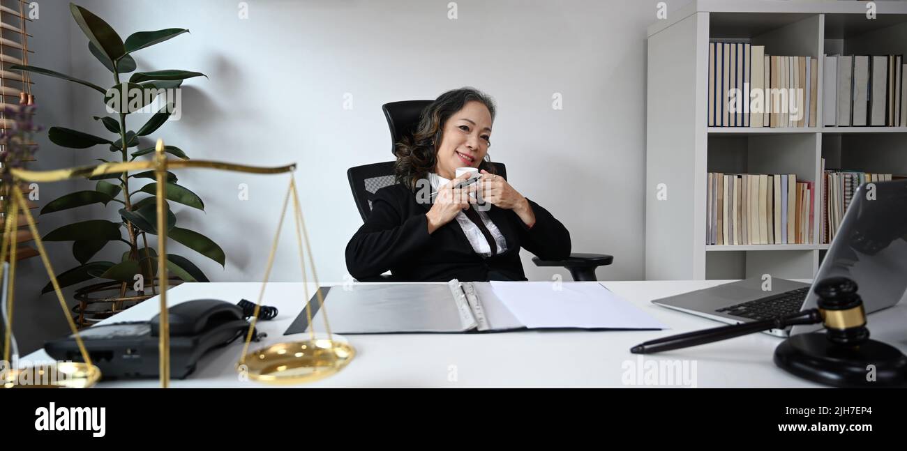 Mature female lawyer drinking coffee, resting at her personal office Stock Photo