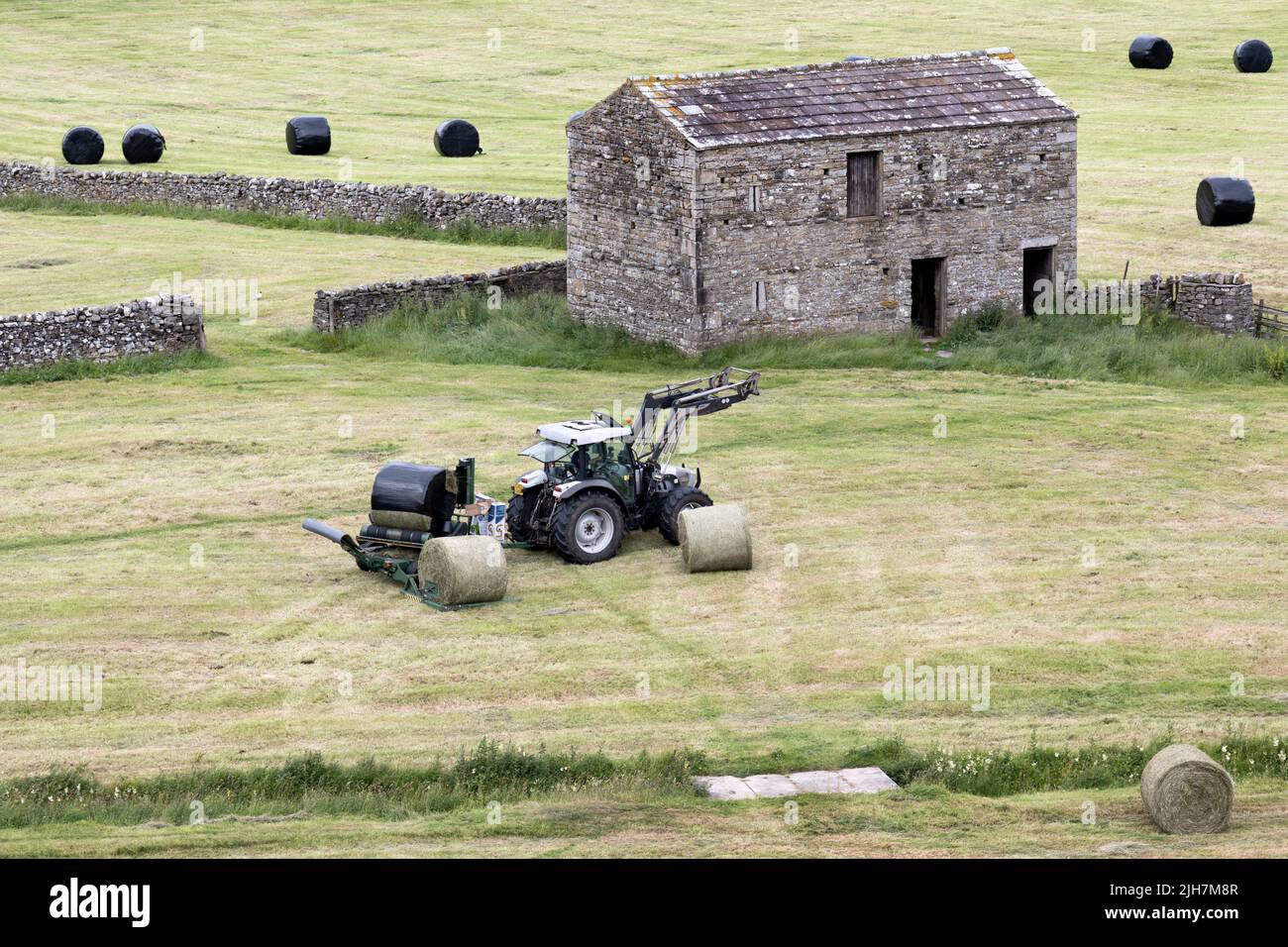 Summer haymaking, Hawes, Wensleydale, North Yorkshire. Round bales are wrapped with plastic to exclude air to make silage or haylage for winter feed. Stock Photo