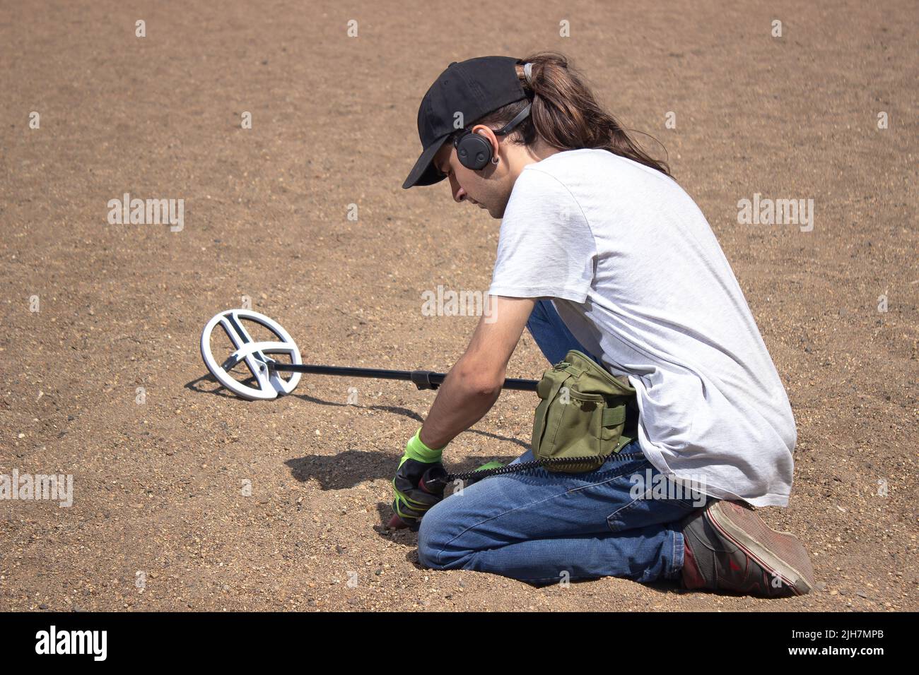 A guy walks along the beach looking for treasure with a wireless metal