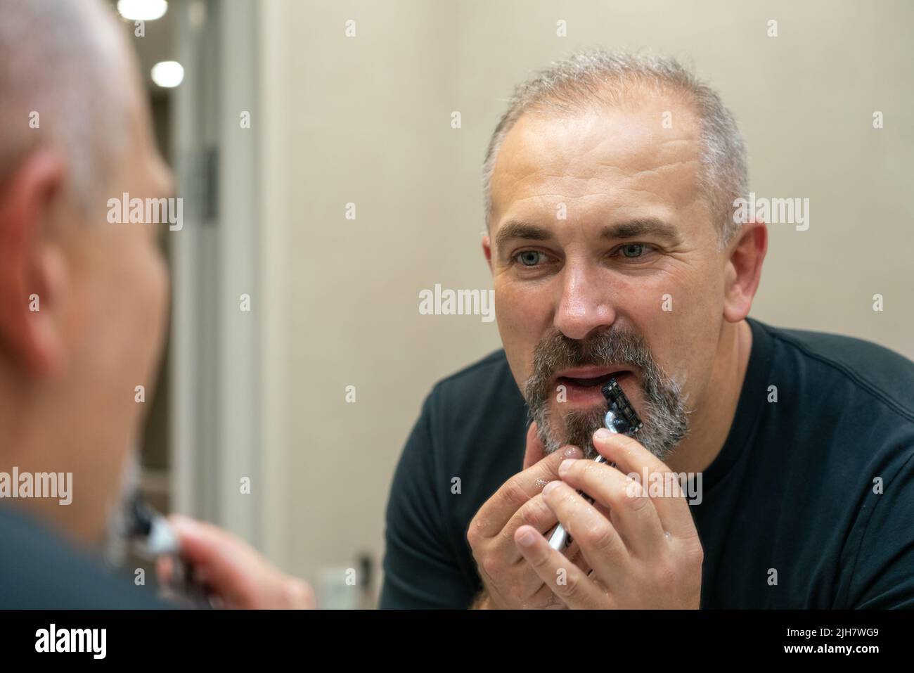 Middle-aged handsome man using razor in bathroom Stock Photo