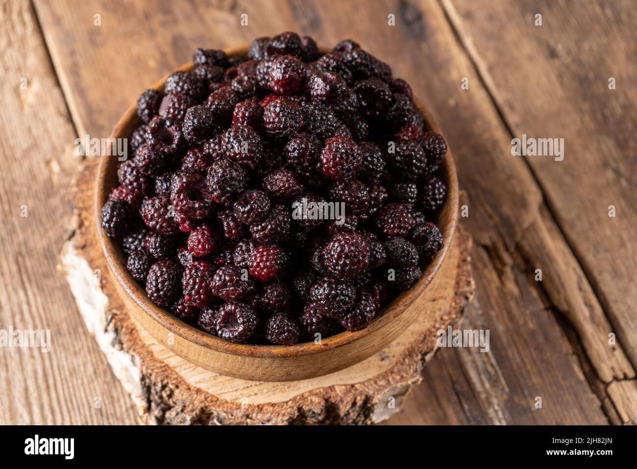 The black berry is a hybrid of raspberries and blackberries. Berries in a wooden bowl on the table. Vitamin summer food. Harvest. Raspberry and blackberry. Black raspberry. Stock Photo