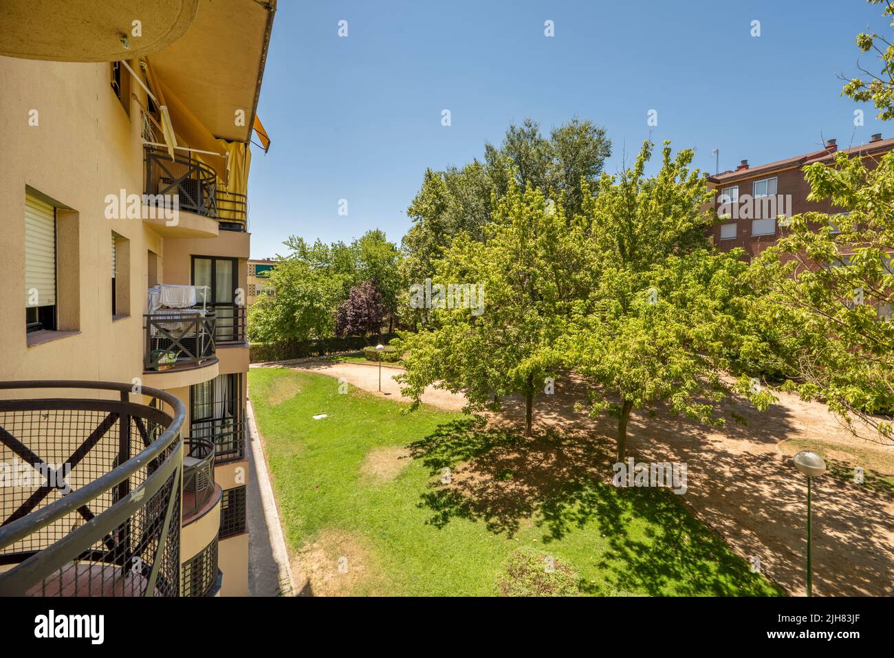 Facades of urban residential houses painted in vanilla-colored mud and windows and black iron and views of a garden with trees Stock Photo