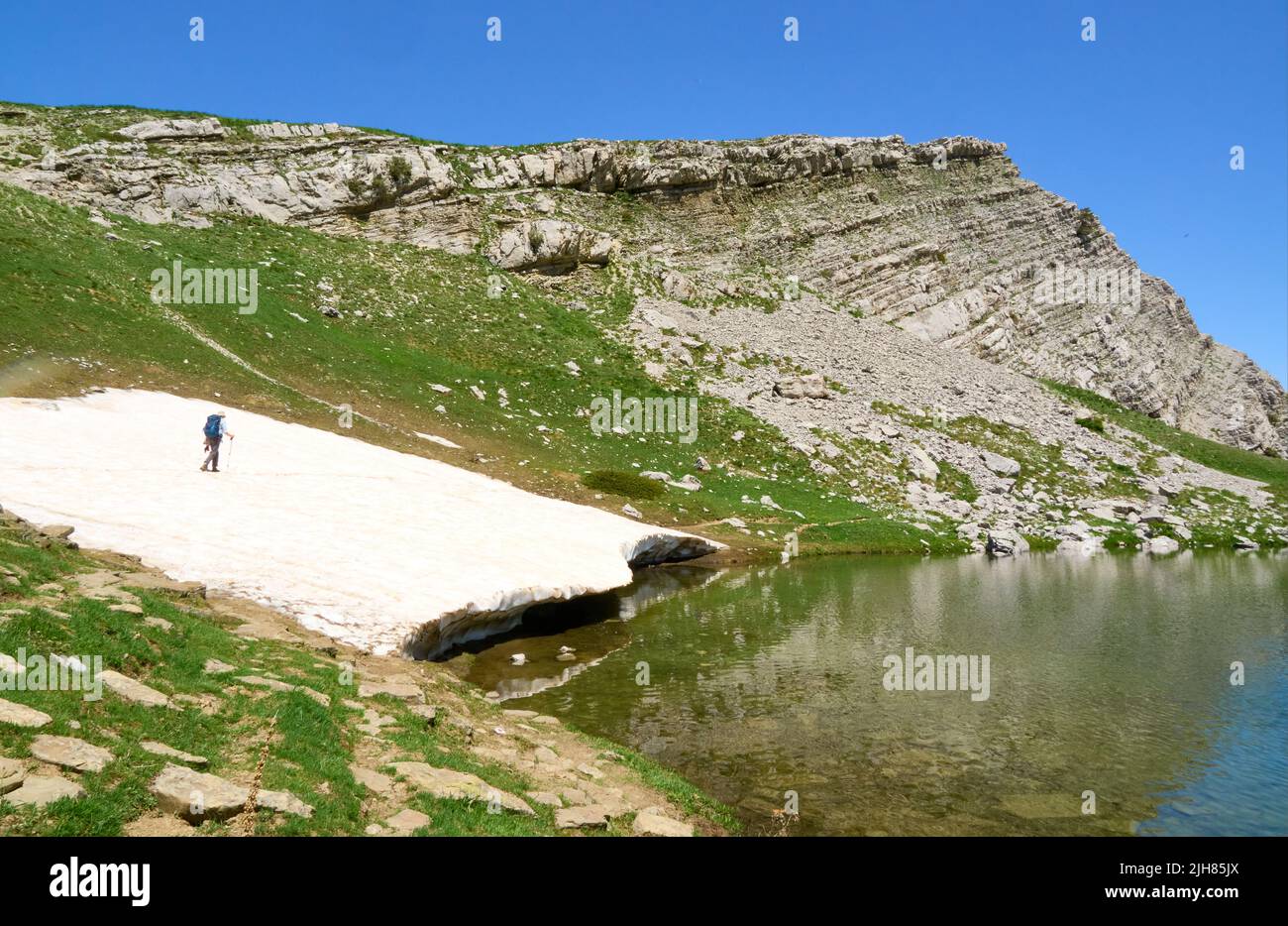 A walker crossing residual snow around Drakolimni the Dragon Lake on Mount Tymphi in the Pindus Mountains of Greece Stock Photo