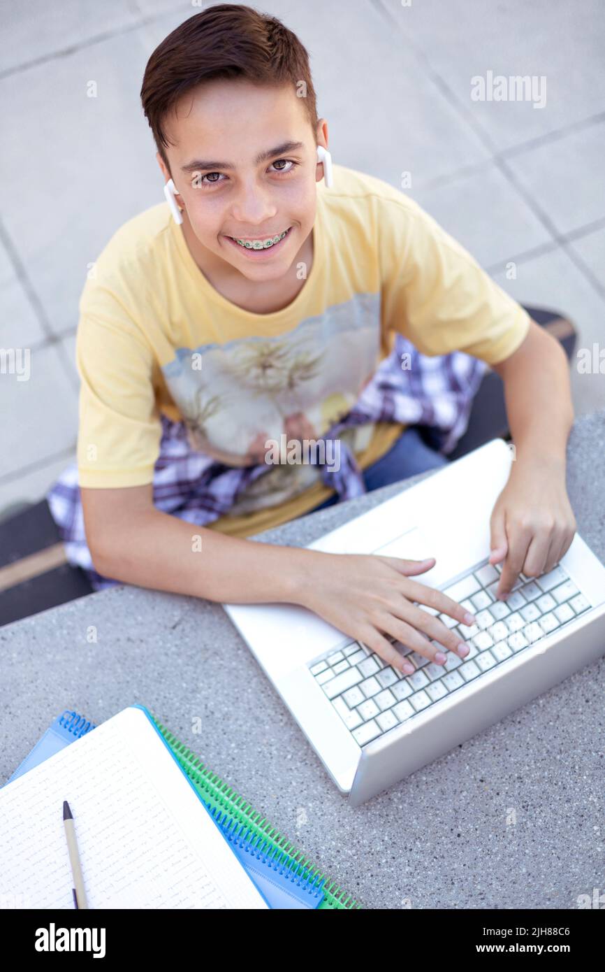 Top view of smiling teenager boy using laptop computer. High school