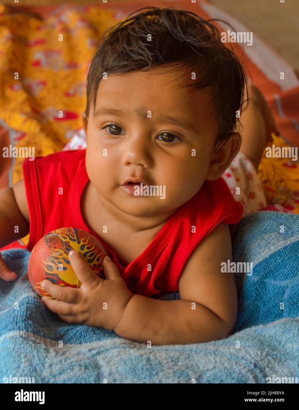 Cute Indian baby playing with ball lying on yellow printed bed sheet