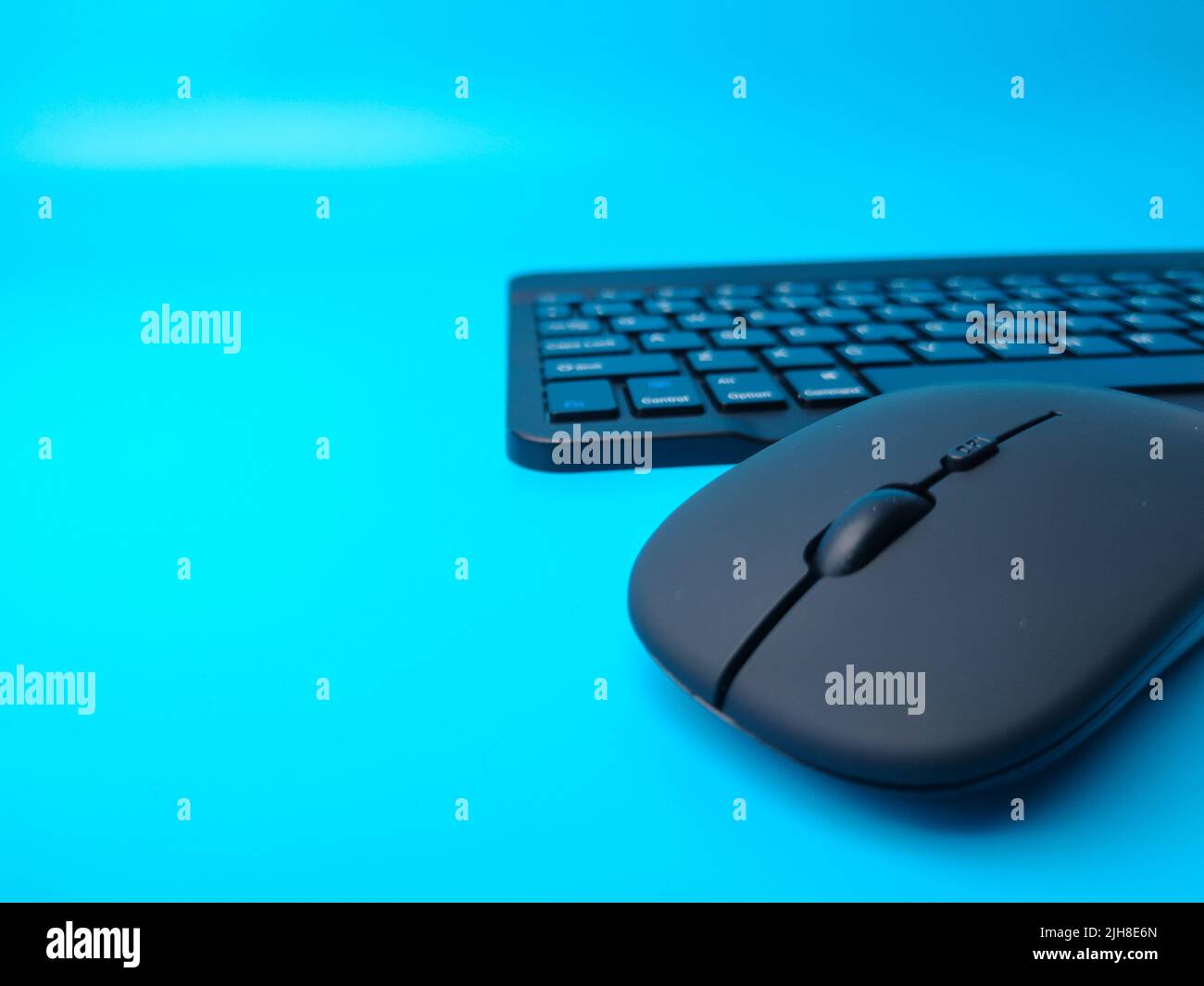 A black Bluetooth wireless keyboard and wireless mouse on a blue background Stock Photo