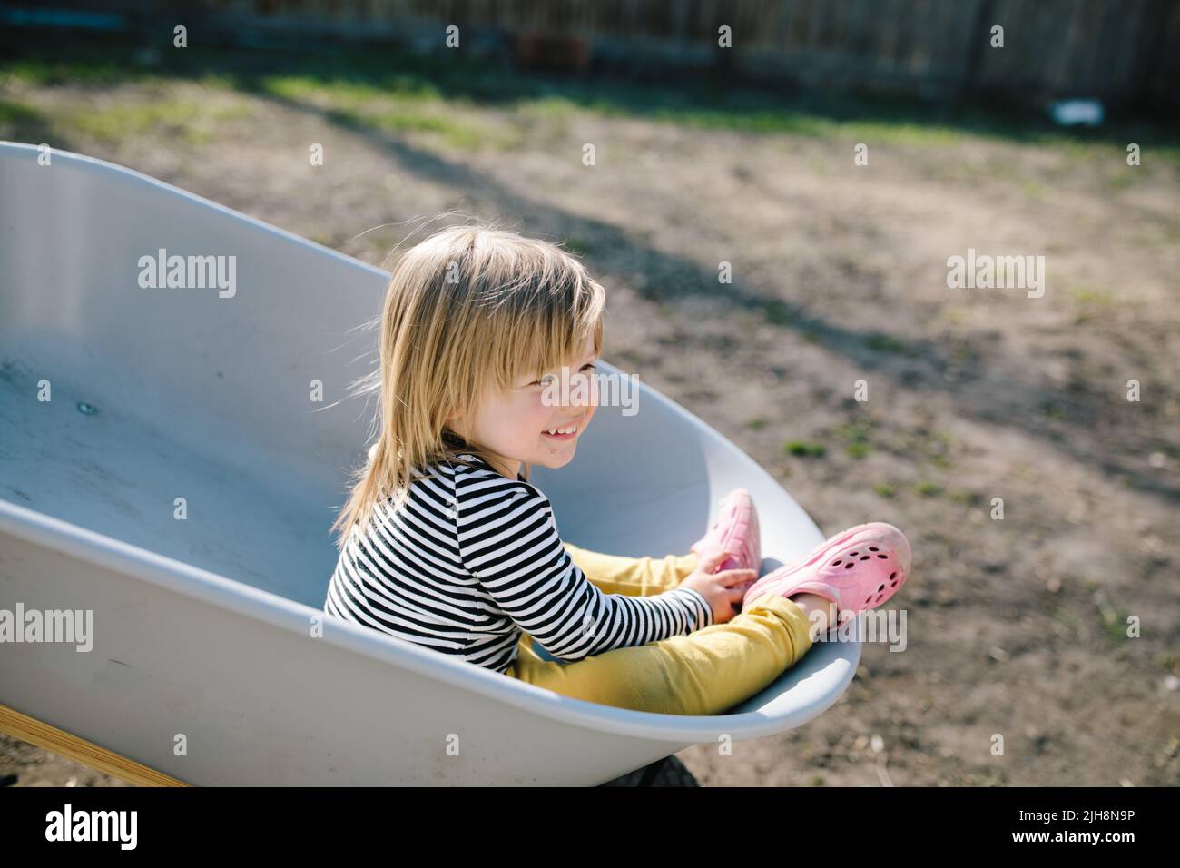 A caucasian little girl having fun riding in a wheelbarrow around the ...
