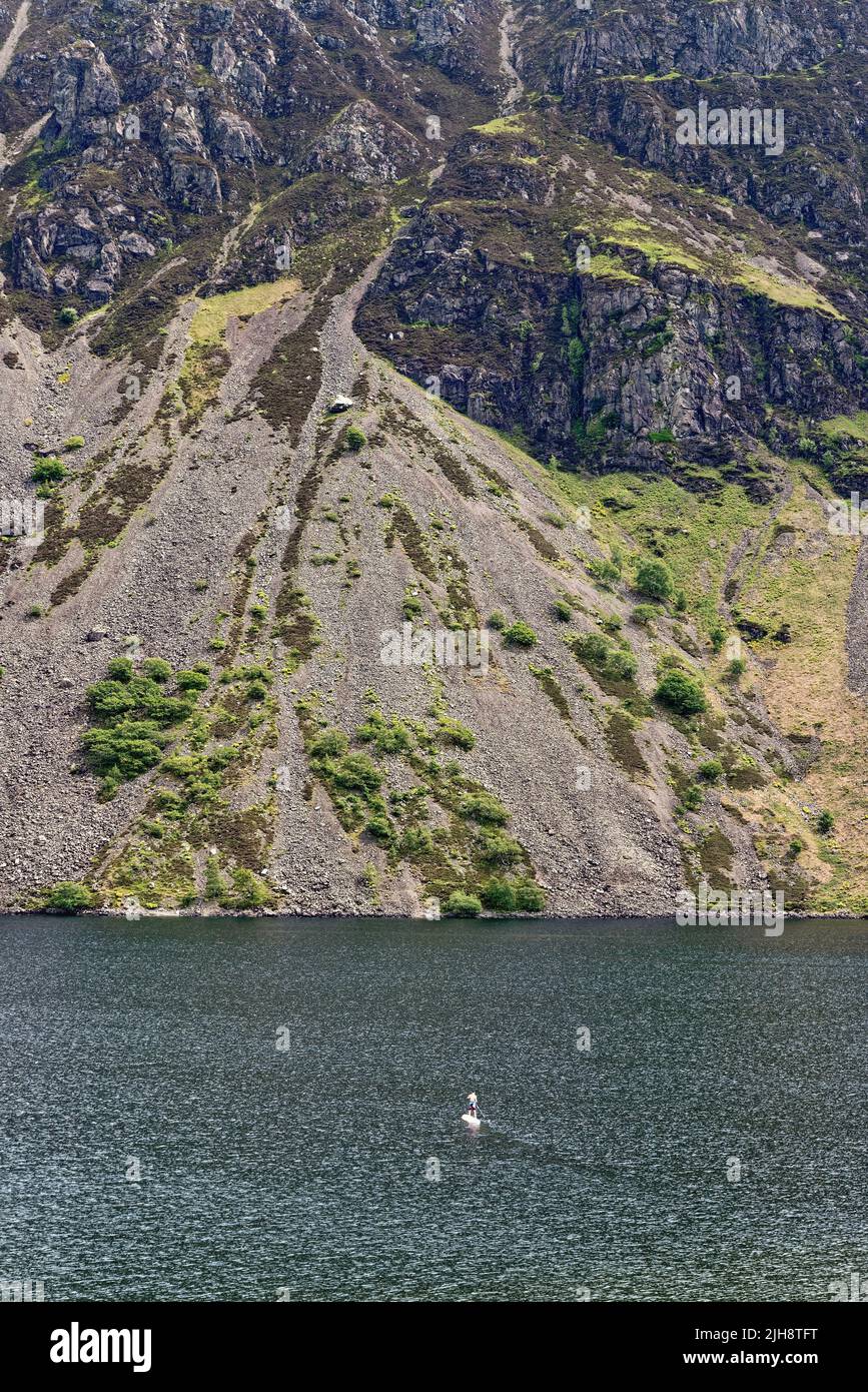 A lone paddleboarder on Wastwater lake dwarfed by the dramatic scree slopes of Illgill Head Wasdale on a summers day Cumbria England UK Stock Photo