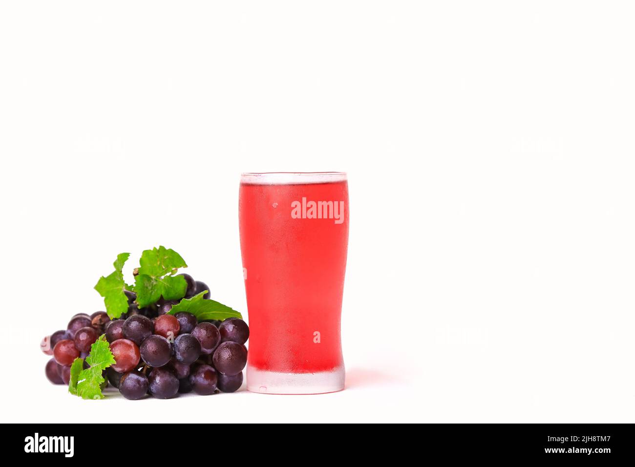 A glass of red grape juice and a bunch of grapes on a white background ...