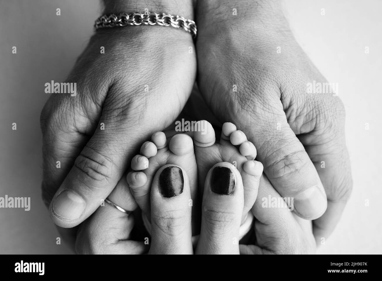 A father and mother hold a newborn baby by the legs. The feet in the